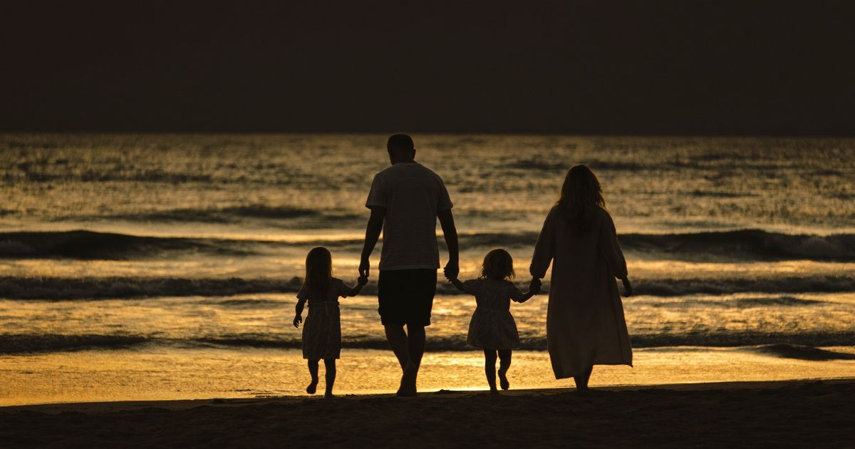 Silhouettes d’un couple et de deux enfants main dans la main sur une plage au coucher du soleil