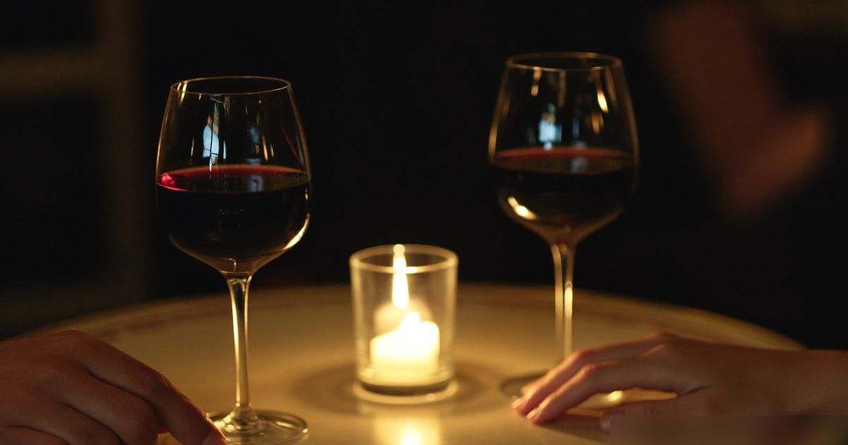 Deux verres de vin et une bougie sur une table de café, deux mains proches l’une de l’autre