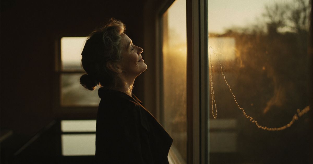 Une femme apaisée, les yeux fermés, face à la lumière du matin près d’une fenêtre